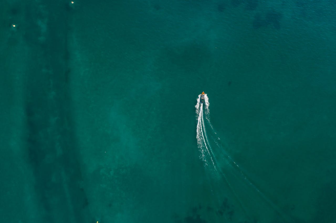 An aerial shot capturing a lone jet ski creating waves on a vast expanse of blue sea.